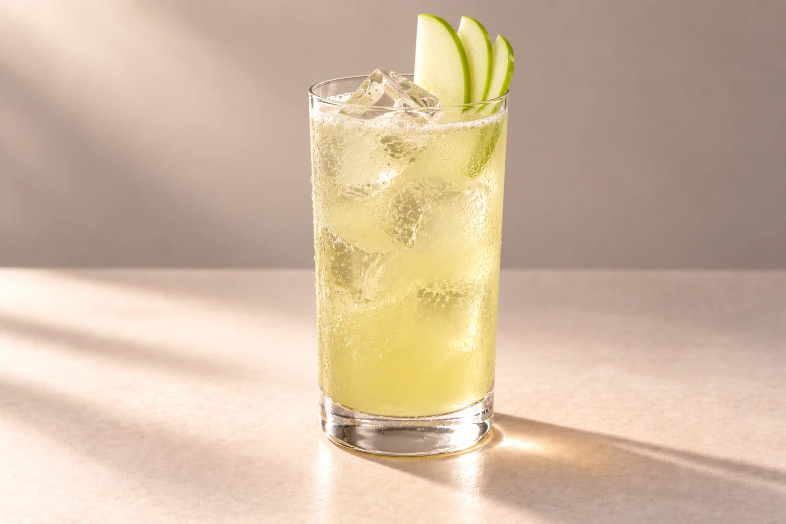 Matcha Orchard Cooler made with Green Tea, Mint & Matcha Chakra Vodka, served over ice in a highball glass with green apple slices on an ivory surface.